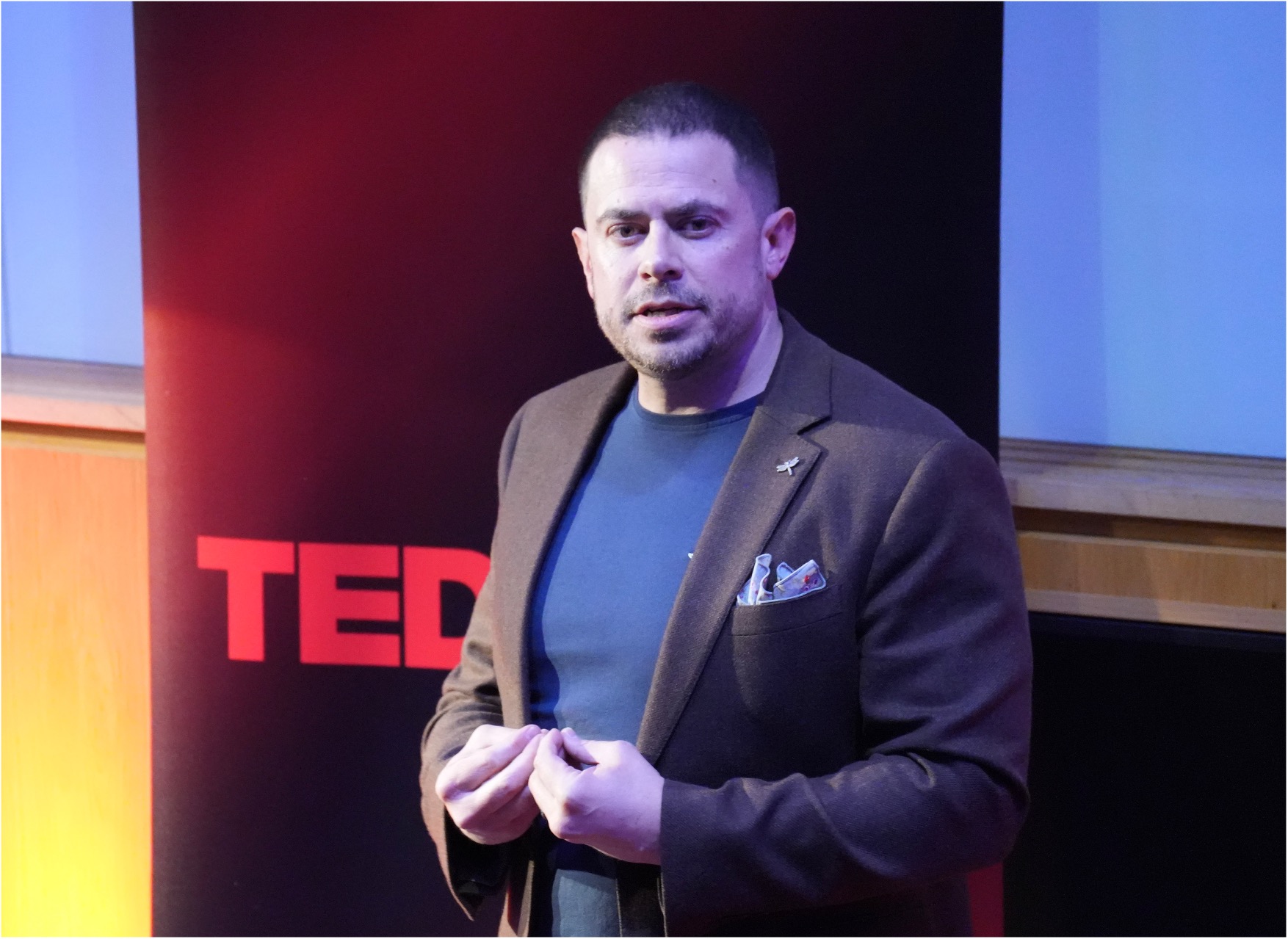 Ian Mullen delivering his TEDx talk on stage, with the red TEDx letters visible behind him